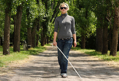 [Photo of a young blind woman walking in the woods]