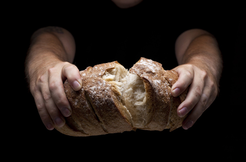 [Photo of a person breaking a loaf of bread]