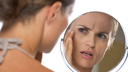 [Photo of a woman examining her face in a mirror]